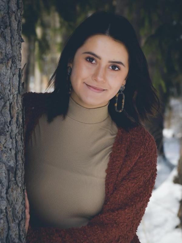 Photo of Juliet Pintos leaning against a tree with a smile