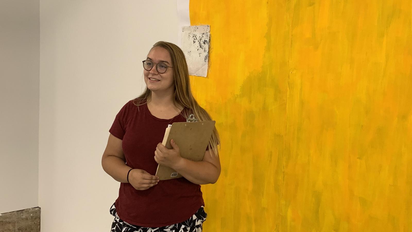 An intern gives an a gallery tour in front of a yellow painting.