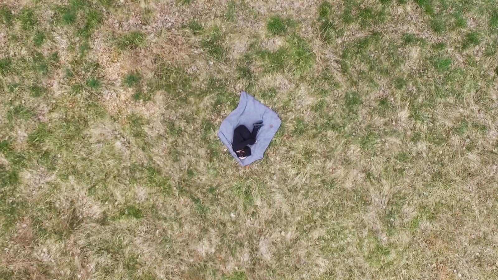 film still of an aerial shot of Person Laying on a blanket in the grass