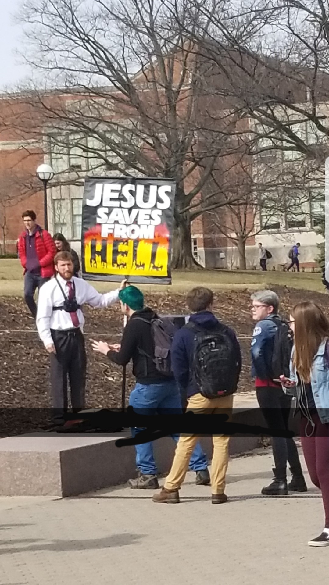 man holding sign in front of group that says "Jesus saves from Hell"