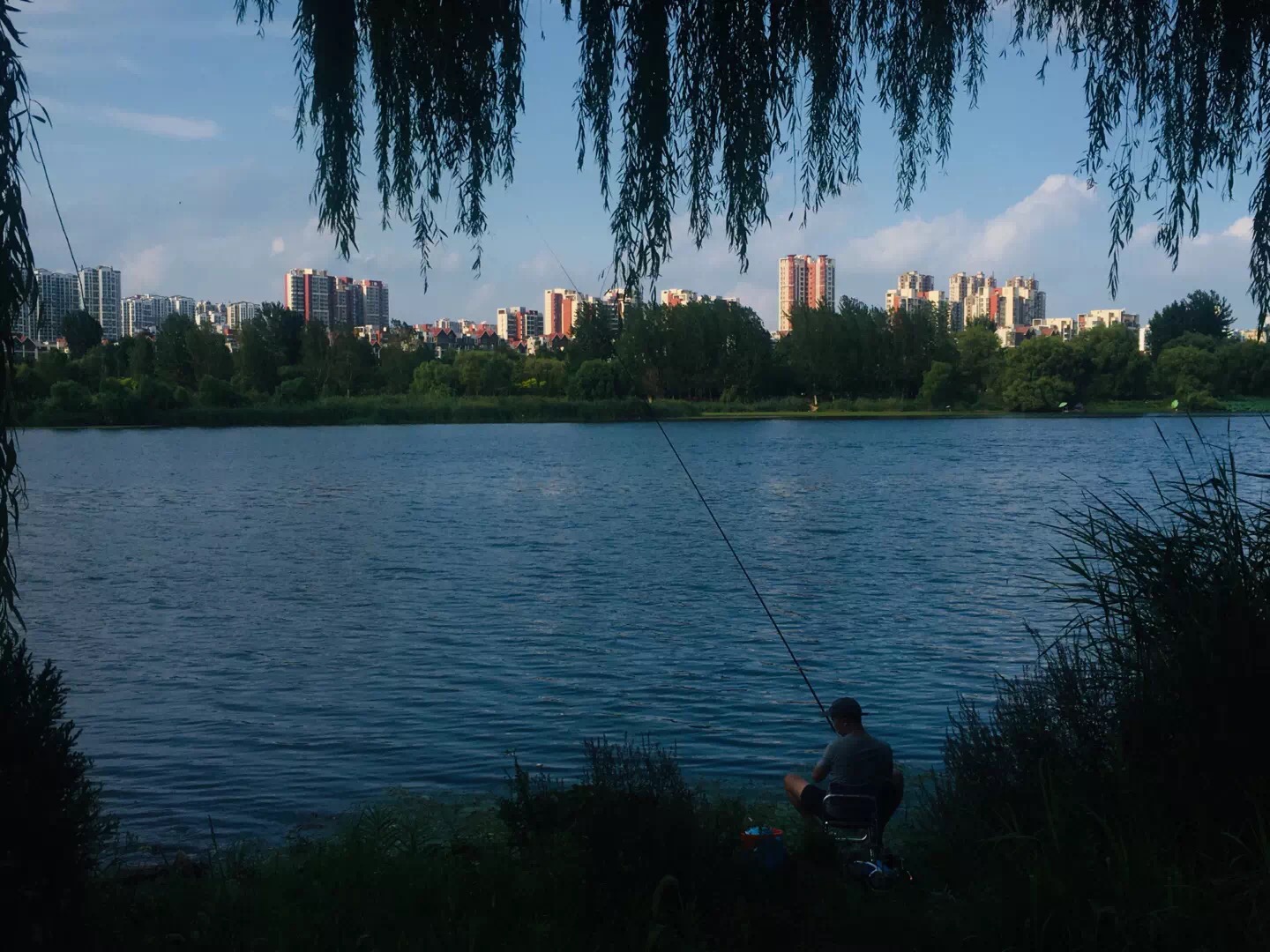 man fishing on lake with city in background