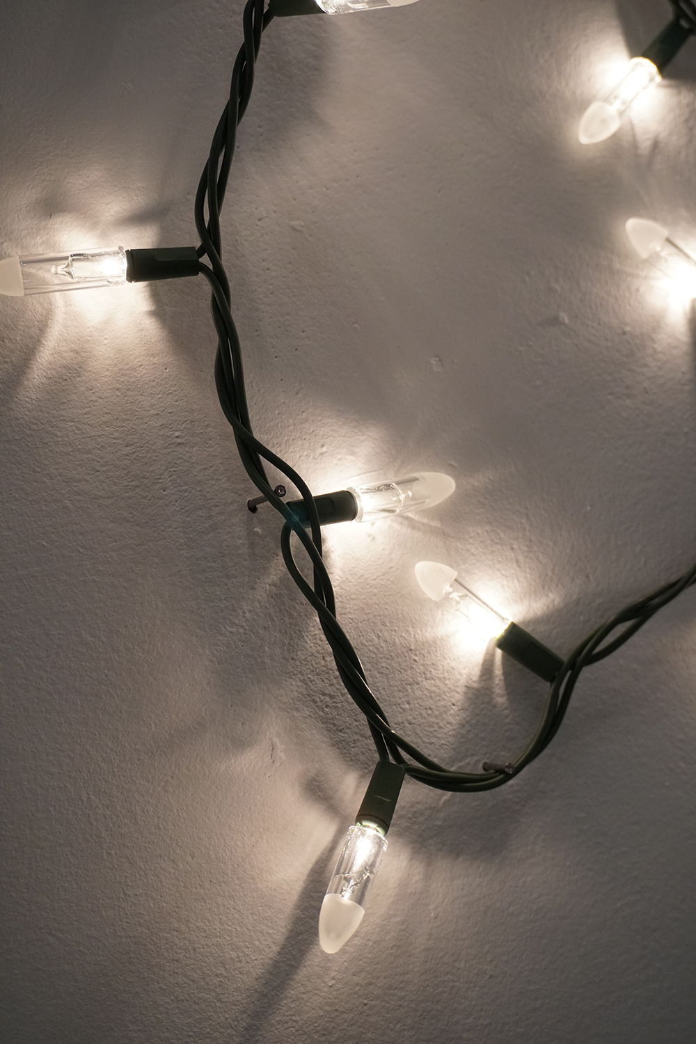 A close-up photograph of string lights showing detail of the handmade glass bulbs attached to the dark colored electrical wiring. The light from the bulbs shines and give off a warm white light.