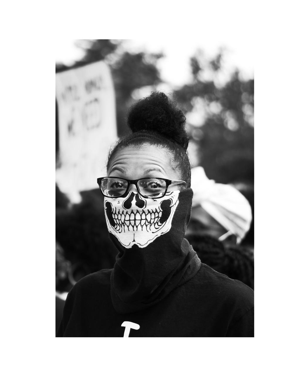 black and white photograph of a woman wearing a skulk mask that covers the bottom half of her face during a march