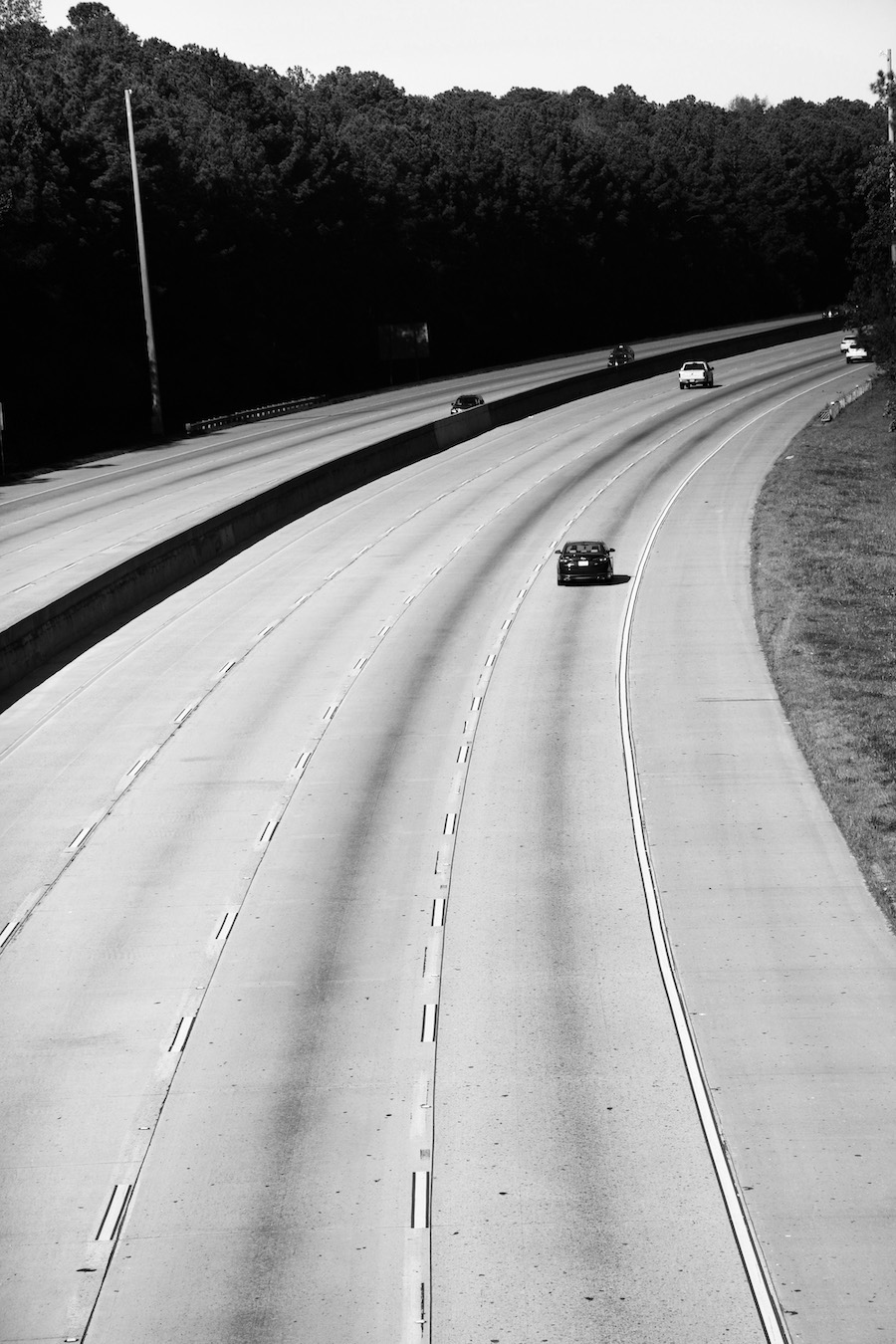 A black-and-white photo of a car driving down a mostly empty highway