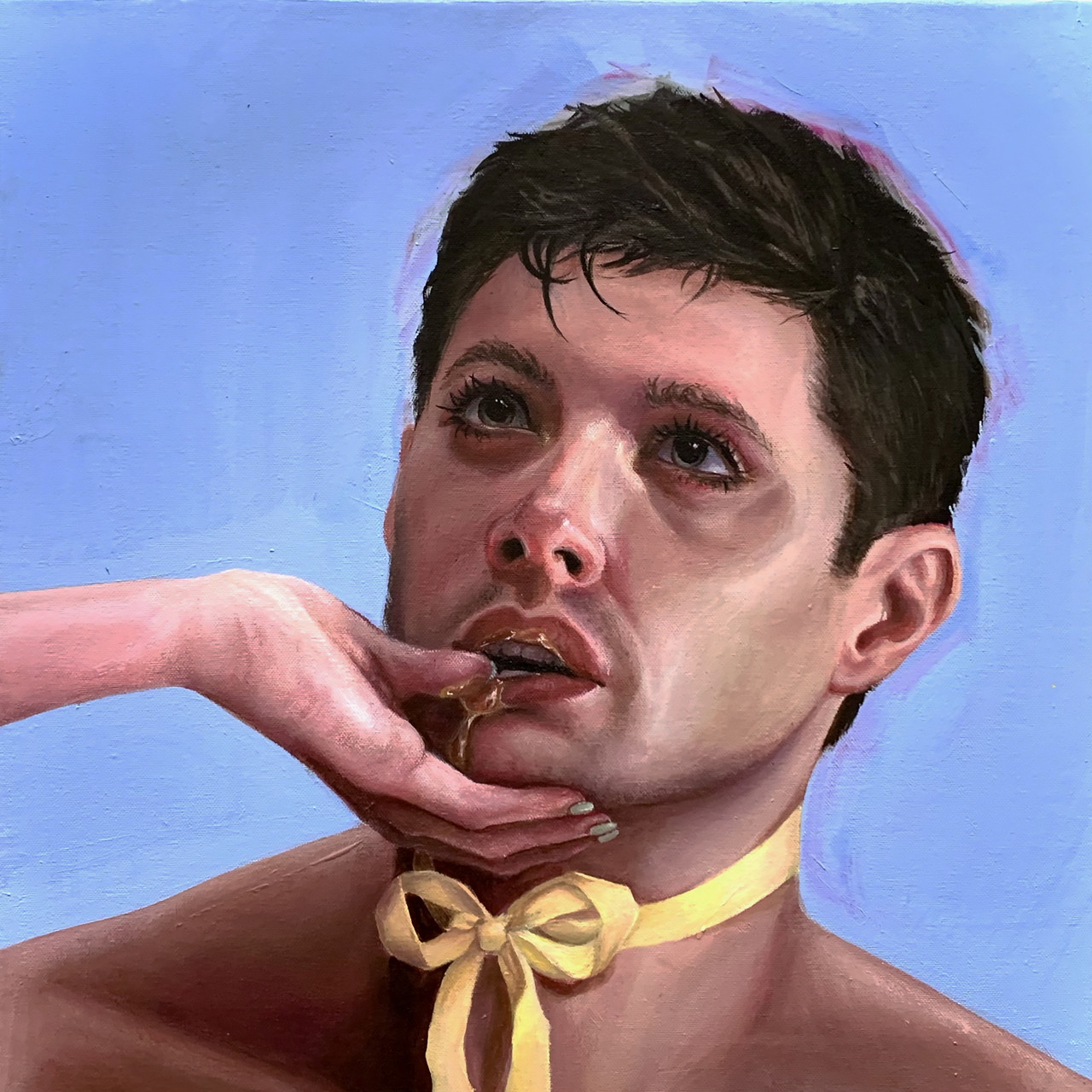 A man with a yellow bow tied around his neck looks up at an unseen woman whose thumb is in the man's mouth, dripping with golden liquid