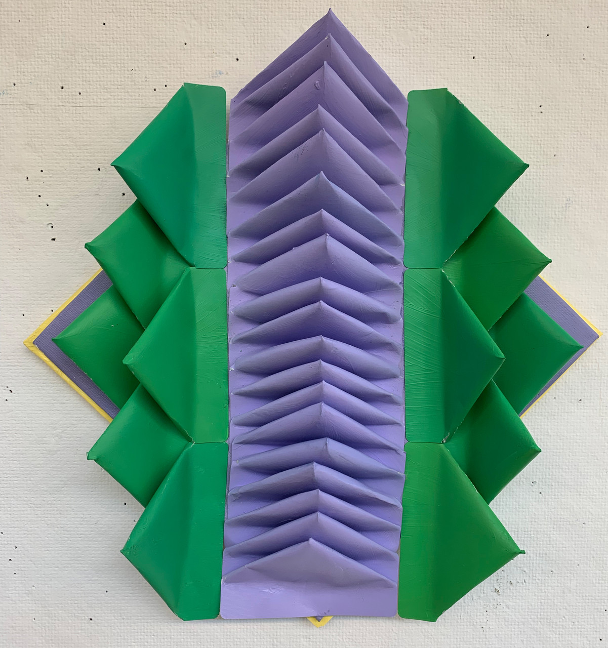 A sculpture composed of multiple purple triangles in a row surrounded by rows of green, purple, and yellow triangles