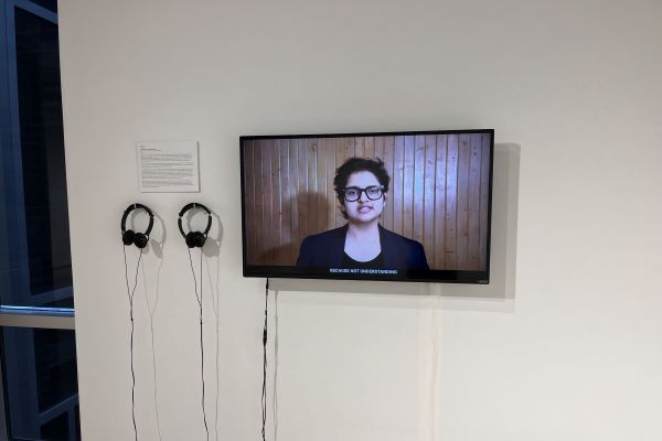 A photo of a flat-screen television mounted on the wall displaying a video performance, there are two pairs of headphones to the left of the television.