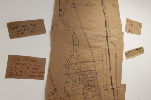 A portion of a map of Columbus is drawn on brown paper, which hangs on the wall. A sign to the left of the map asks "What are the sounds of our city?"