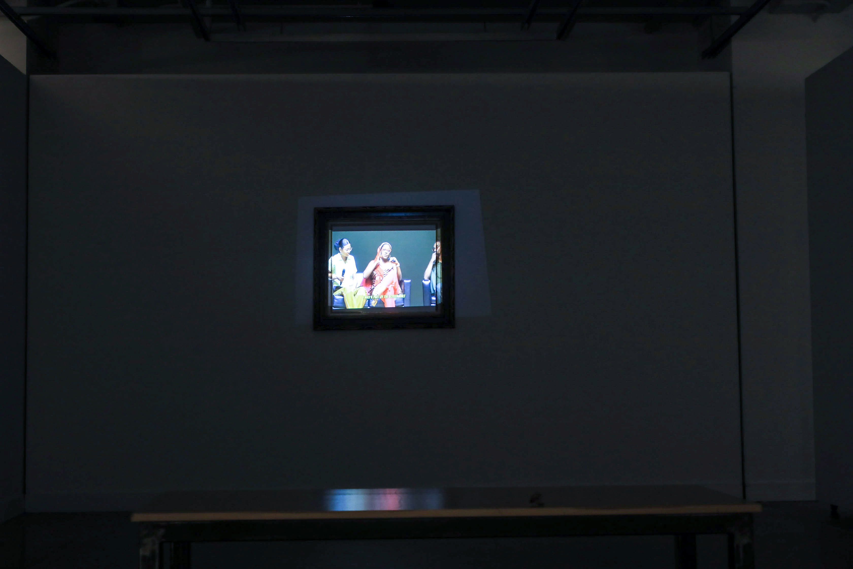 A video projected into a frame on the wall with a bench to sit on.