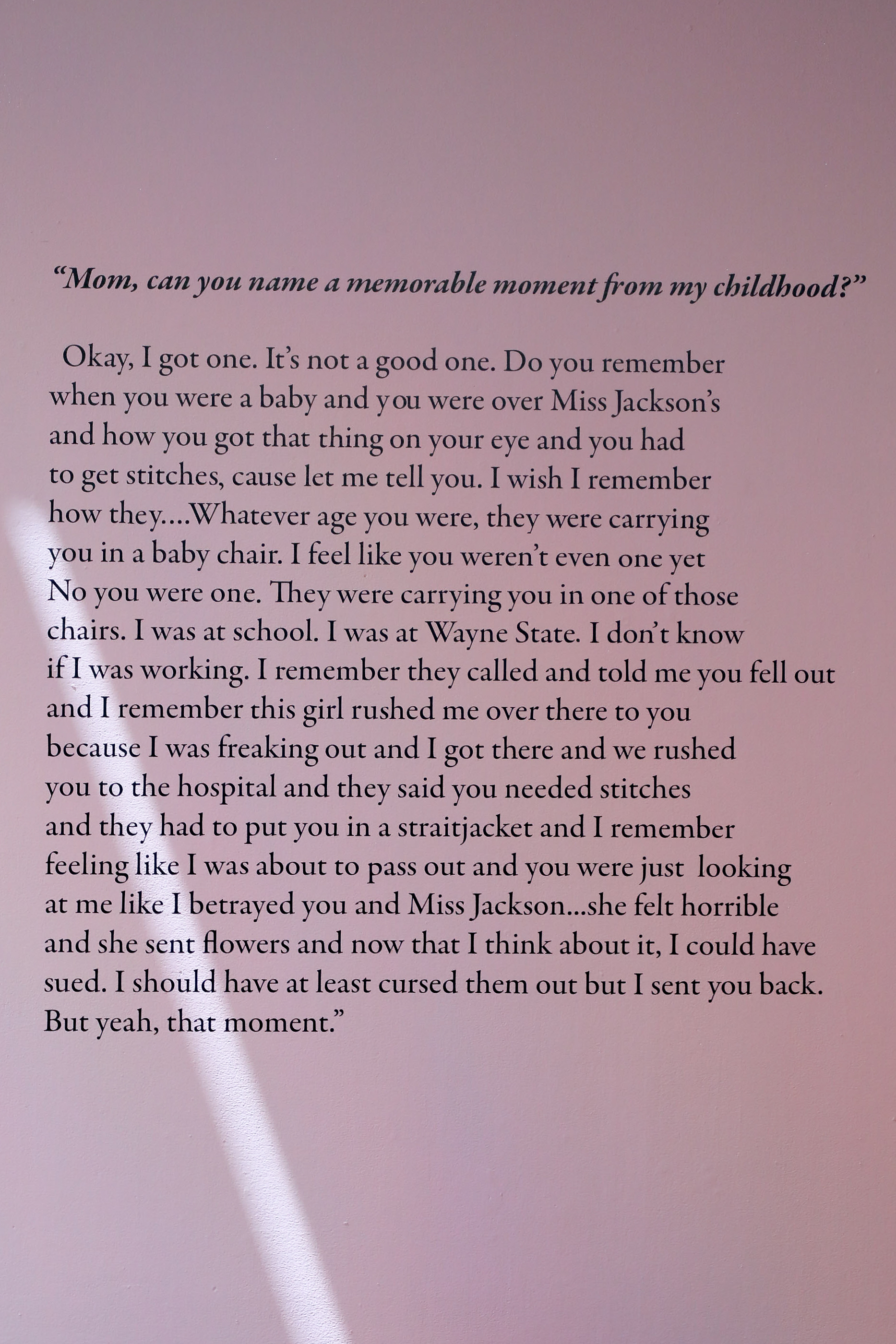 A pink wall with an excerpt of an interview with Ajanaé and her mother. The excerpt says, “Mom, can you name a memorable moment from my childhood? Okay, I got one. It’s not a good one. Do you remember when you were a baby and you were over Miss Jackson’s and how you got that thing on your eye and you had to get stitches, cause let me tell you. I wish I remember how they….Whatever age you were, they were carrying you in a baby chair. I feel like you weren’t even one yet No you were one. They were carrying yo