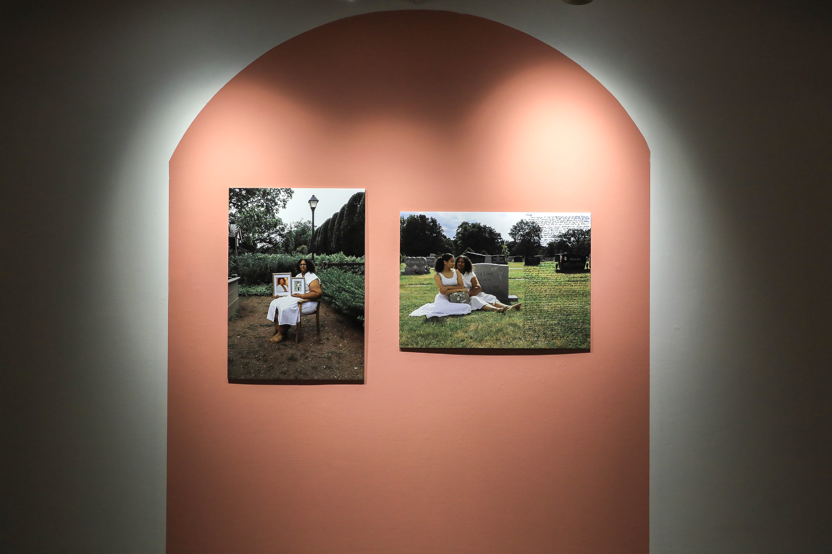 Two color photos on top of a red-orange painted shape: the one of the left features an older black woman wearing white, sitting in a garden holding two pictures. The one of the right depicts Iyana and the older woman wearing white, sitting next to a gravestone and holding a stone with her sister’s picture and epitaph. There is writing on the right side of the right picture