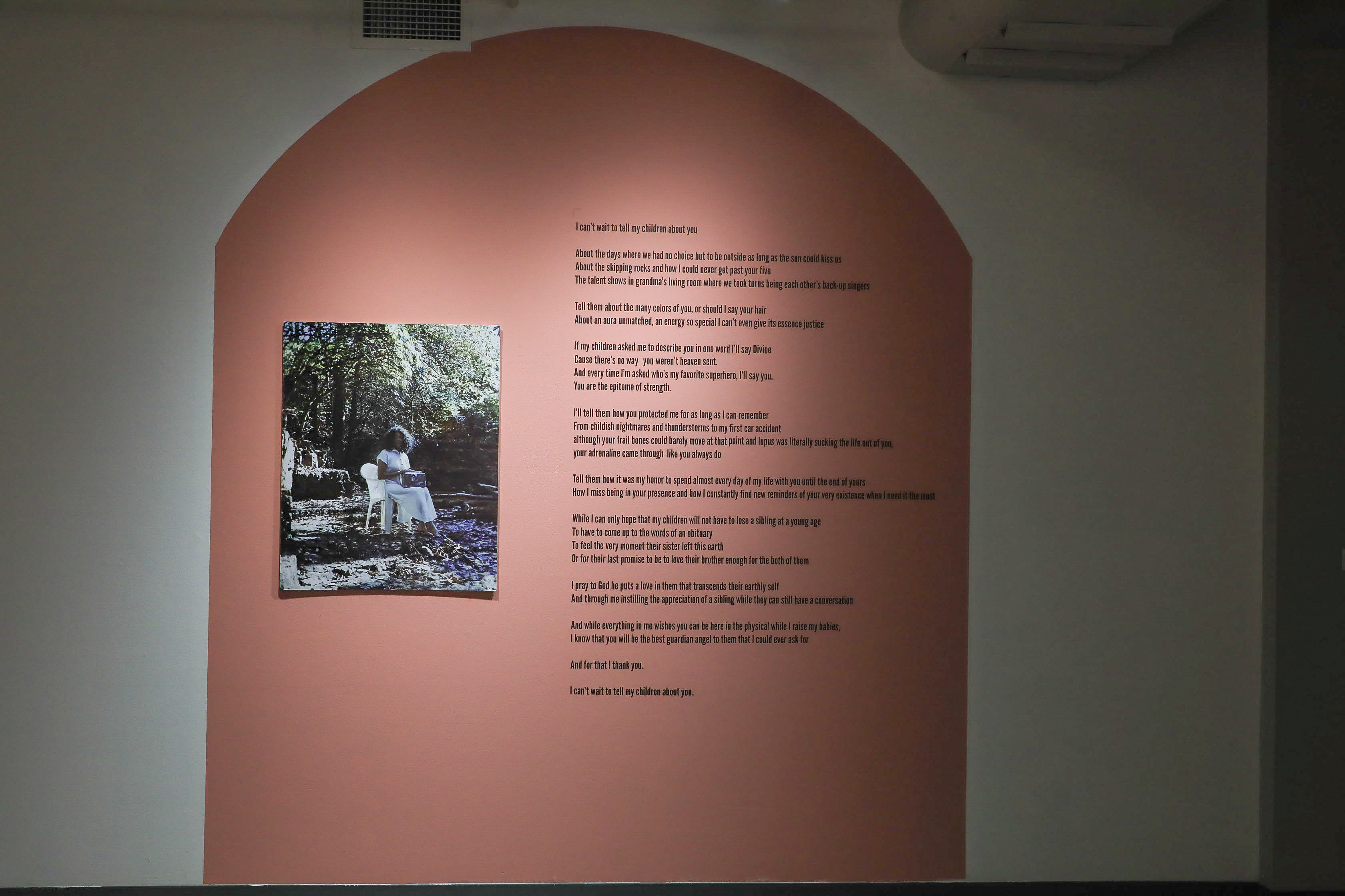 There is a color photo on top of a red-orange painted shape: the photo shows Iyana dressed in white sitting in the woods holding a stone with her sister’s picture and epitaph. To the right of the photo is a poem.