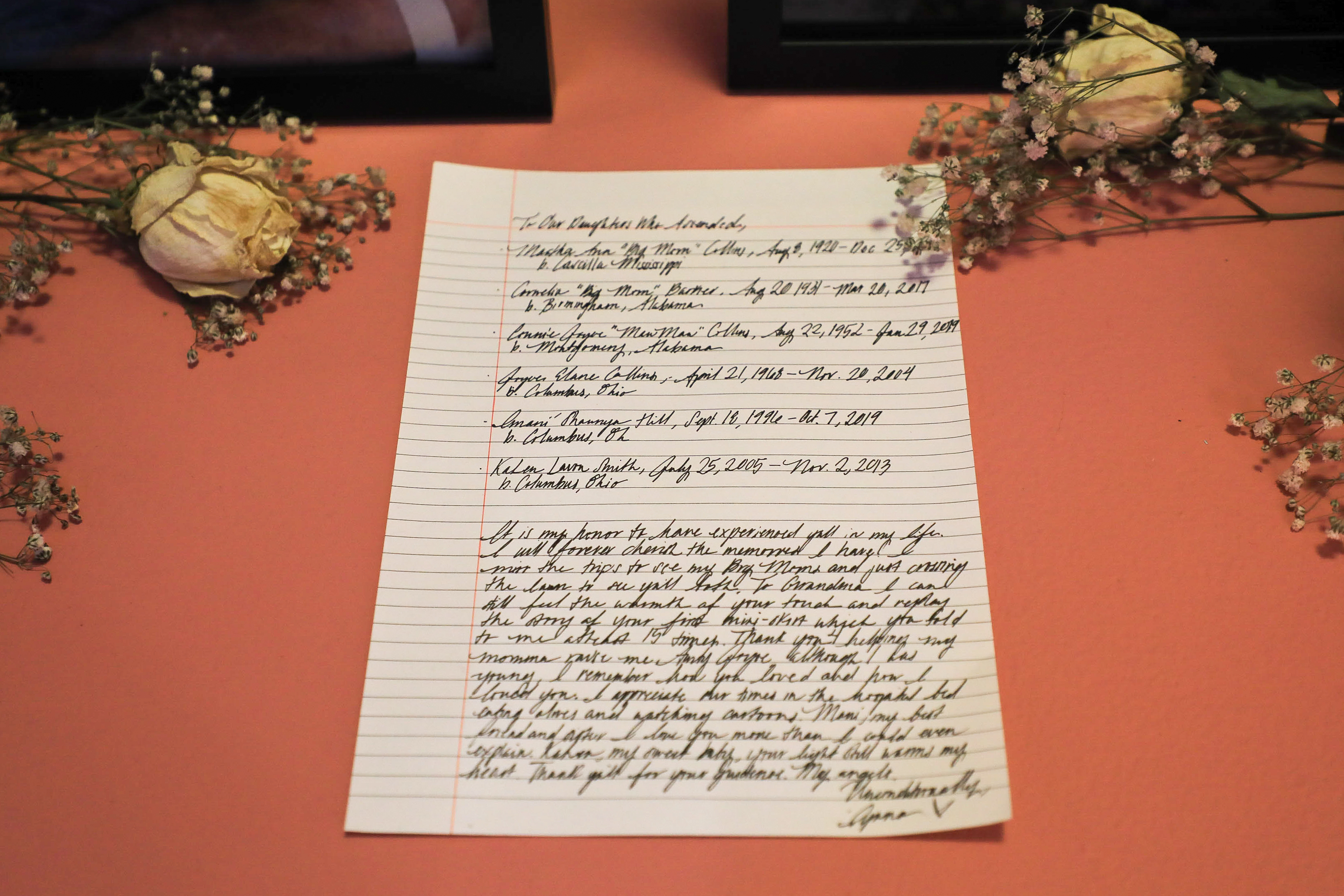 A letter between framed photos and flowers on a red-orange box. 