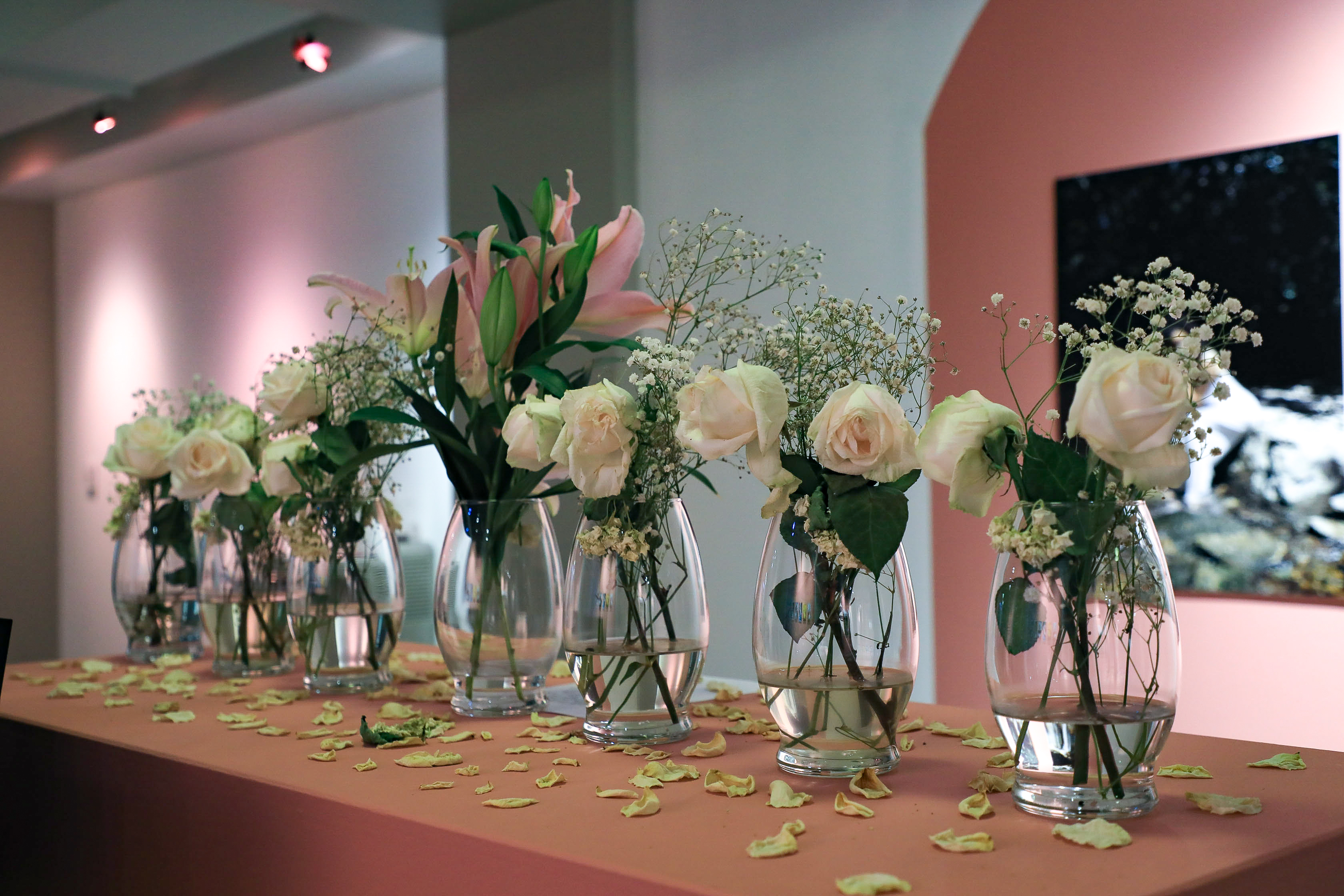 A red-orange box with seven vases filled with flowers. The box has petals all over it. 