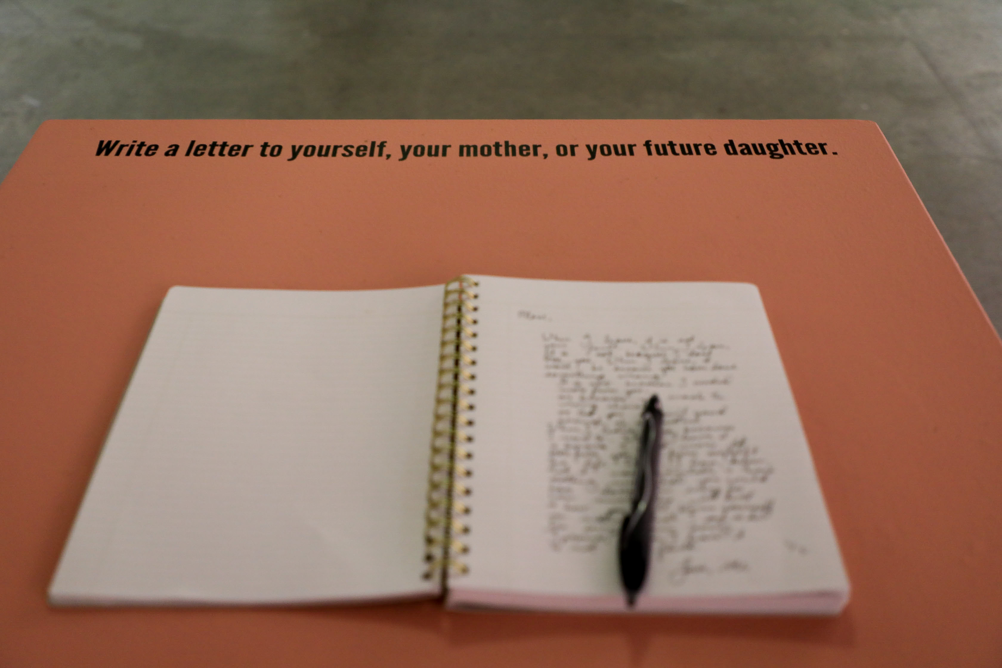 A red-orange box with a notebook and pen and text up top that says, “Write a letter to yourself, your mother, or your future daughter."