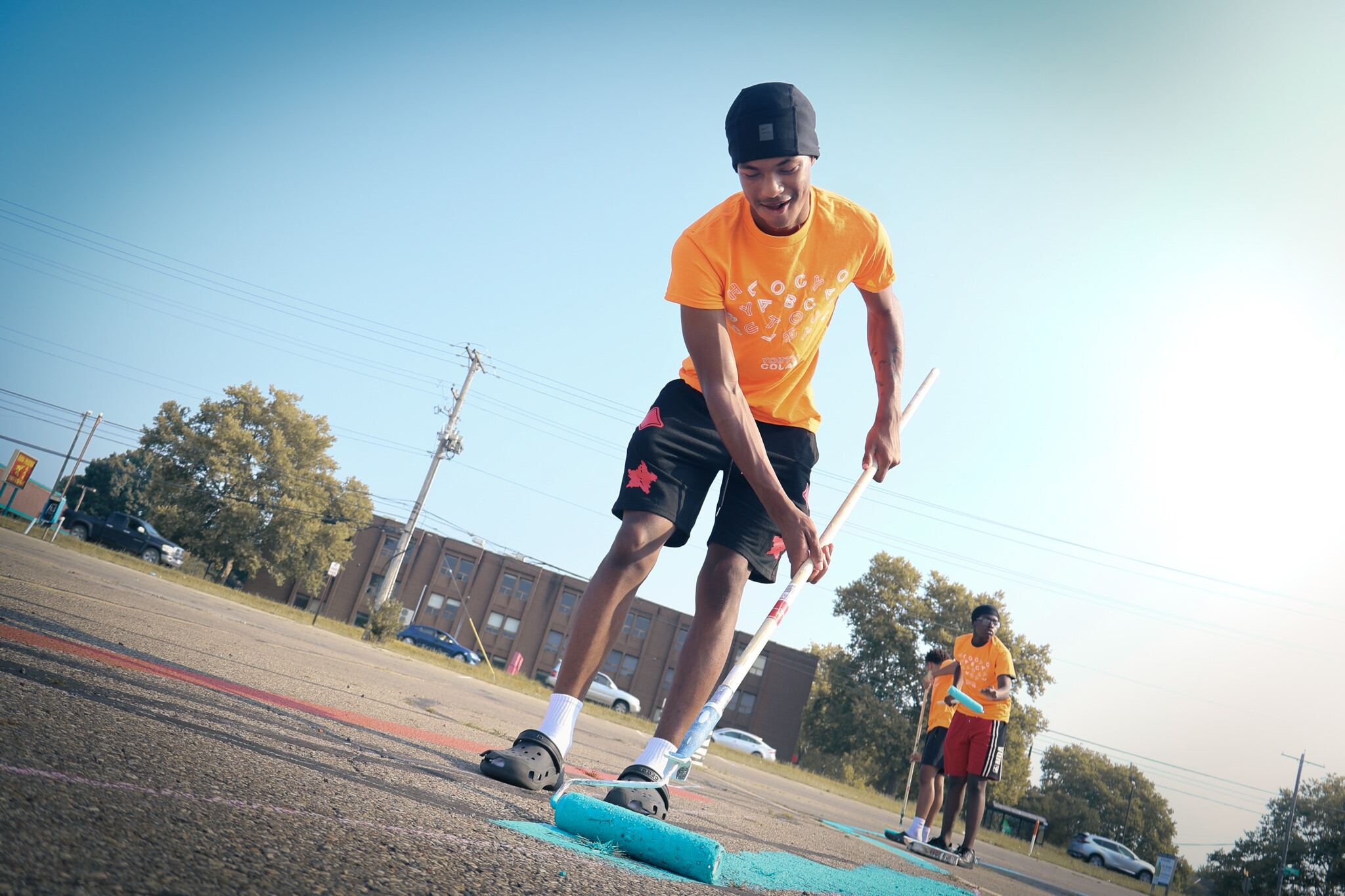 A male student in a yellow shirt colorfully painting the ground with a roller