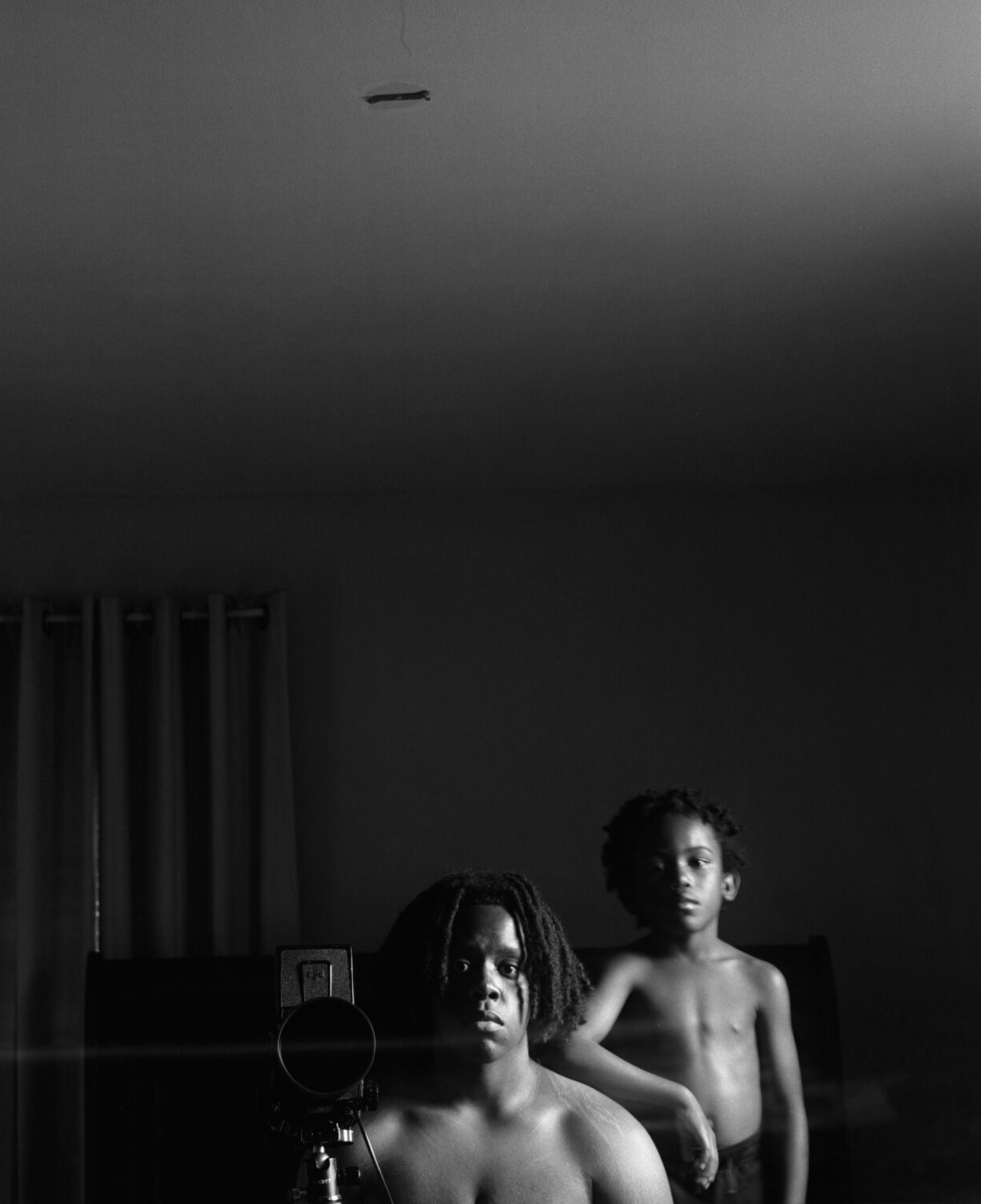 Black and white photo of two brothers in front of a mirror, one young and the other in their 20s. The older brother has scars