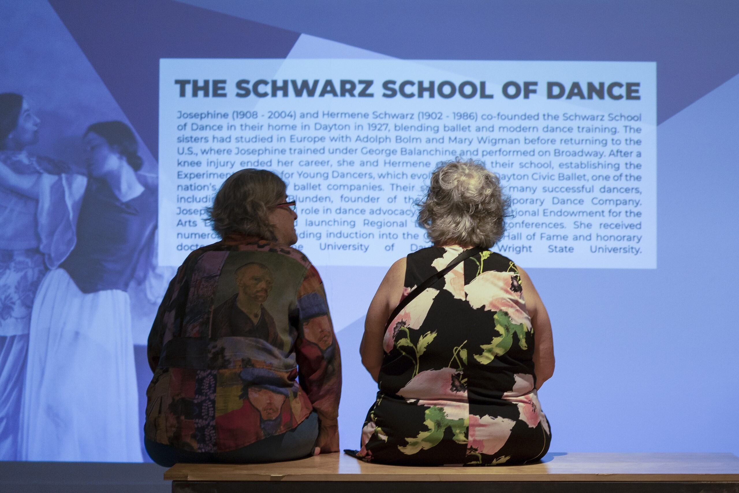 two visitors in front of a projected slide of information about the schwarz school of dance