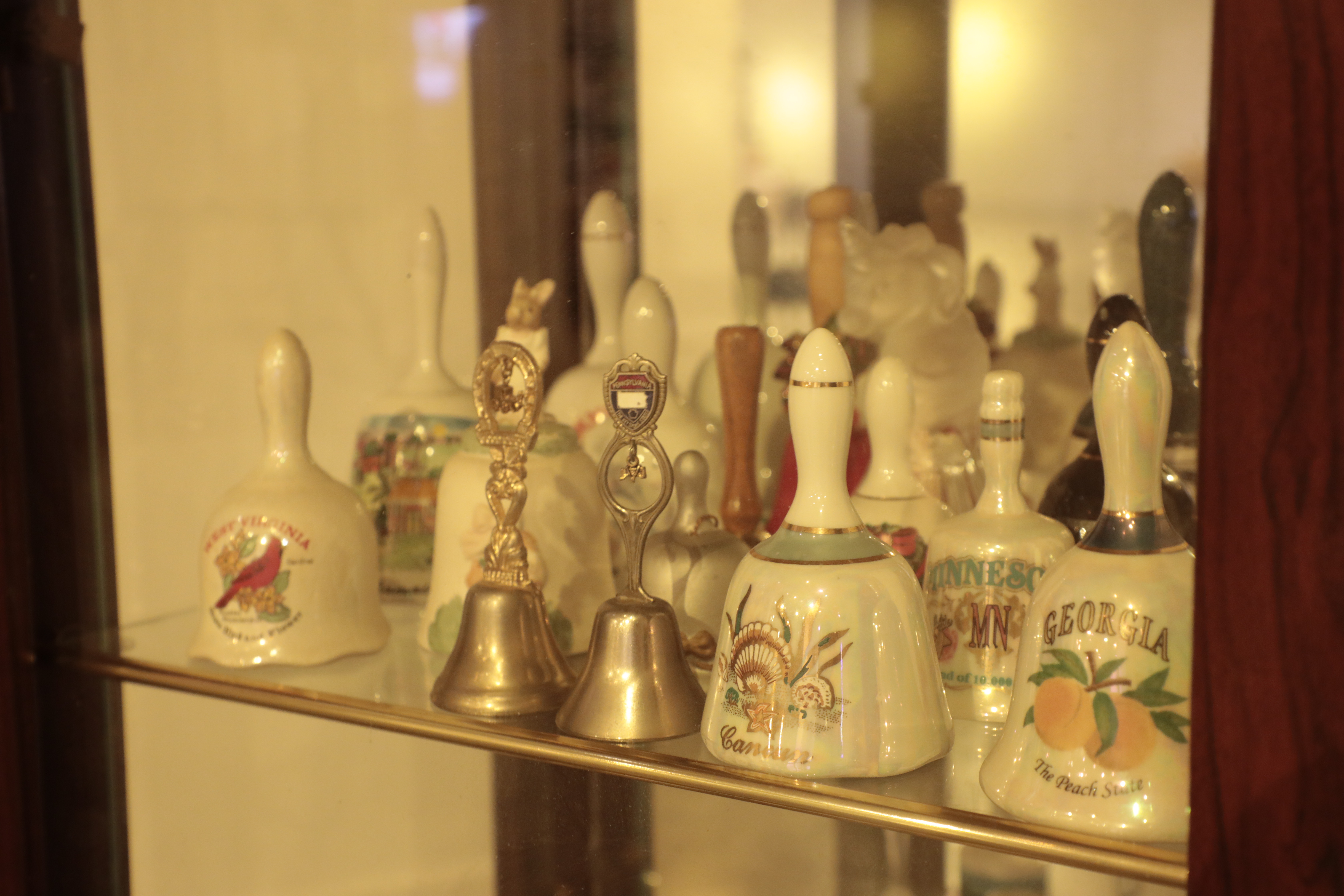 Hand held bells in various sizes sitting on a glass shelf inside a case. 