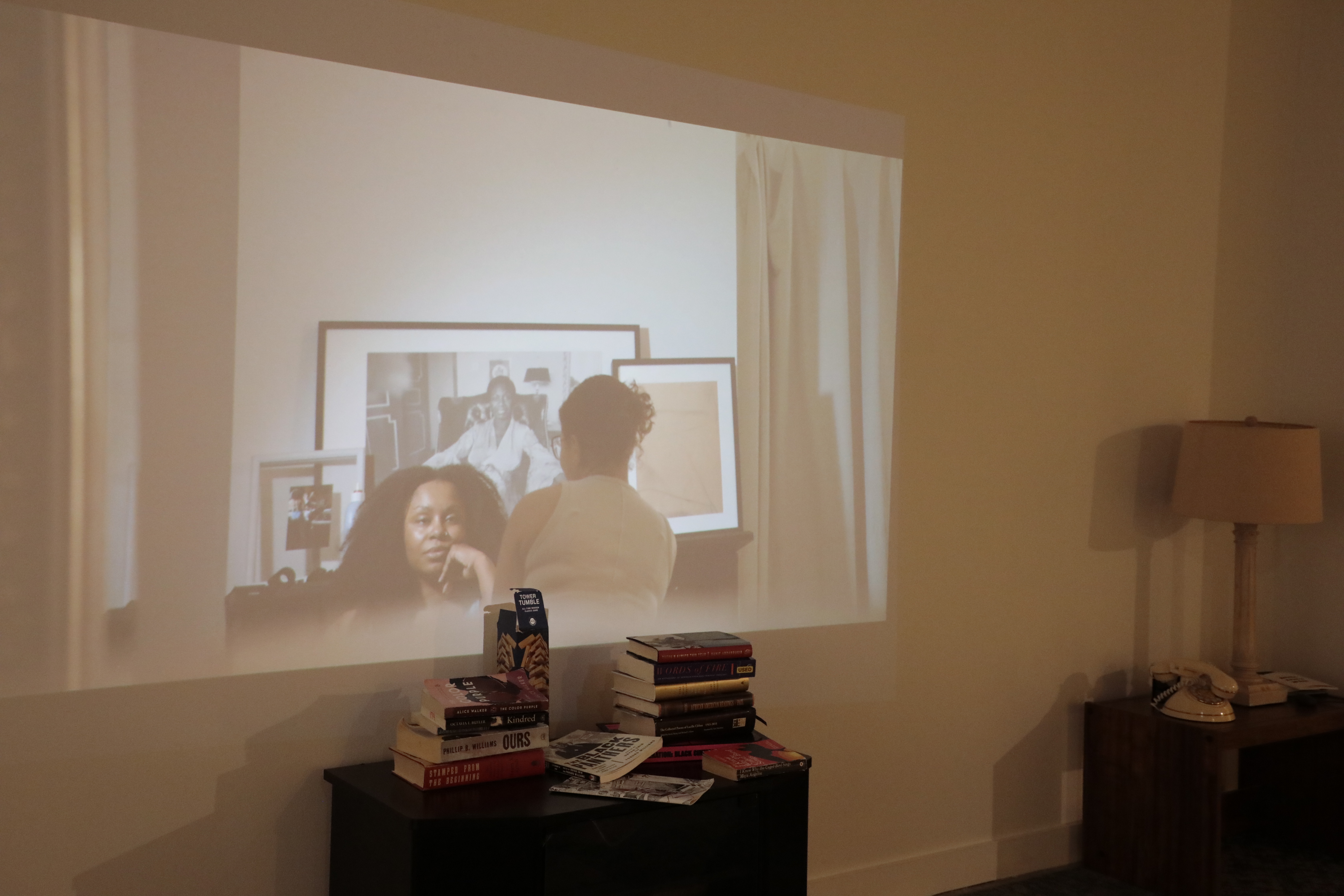 A projected film onto the wall shows two women - one staring into the screen and the other with her back to the audience. 