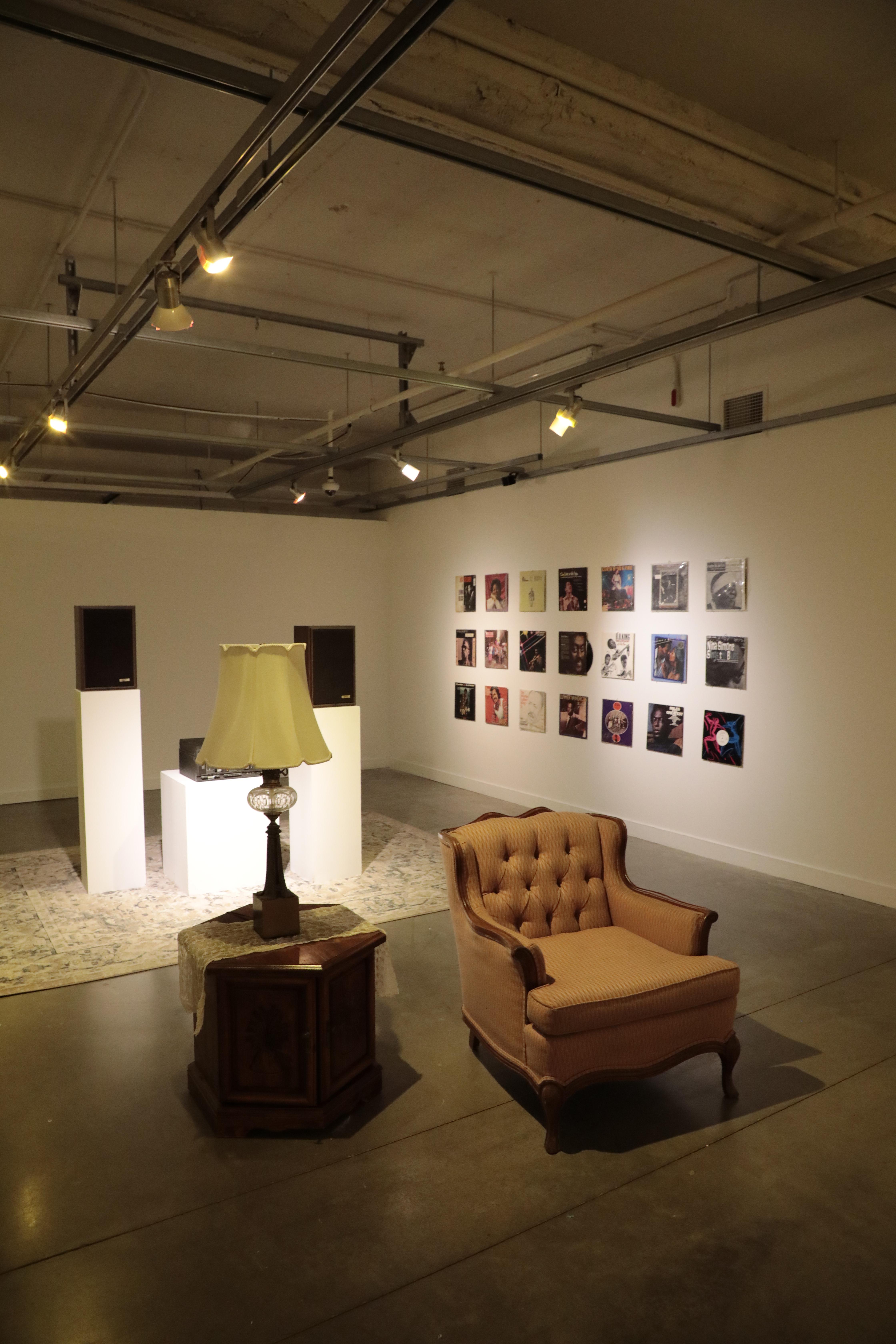 Two large speakers are behind a chair and lamp. The wall holds a variety of vinyl album covers