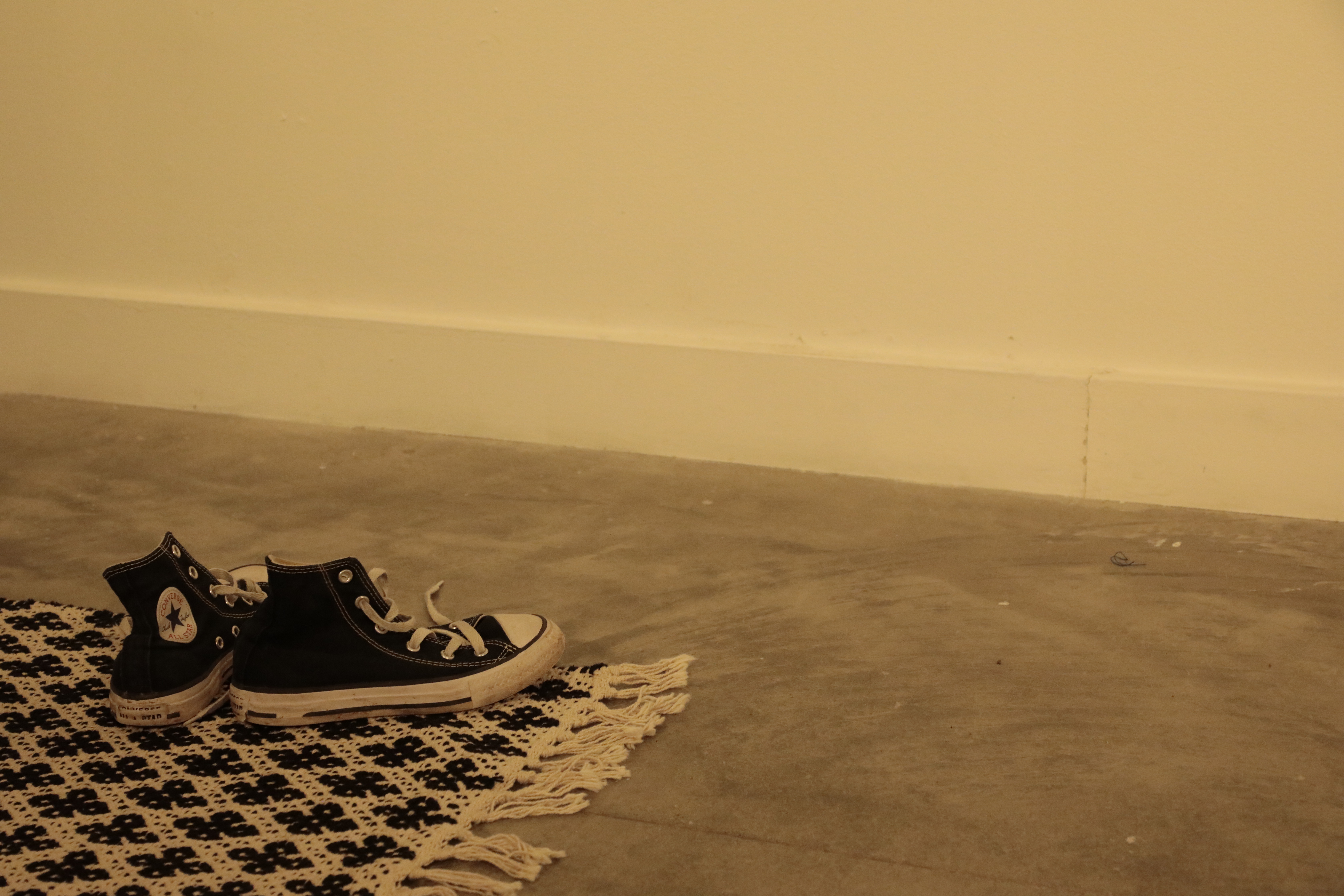 Two converse shoes sit on the corner of a rug. 