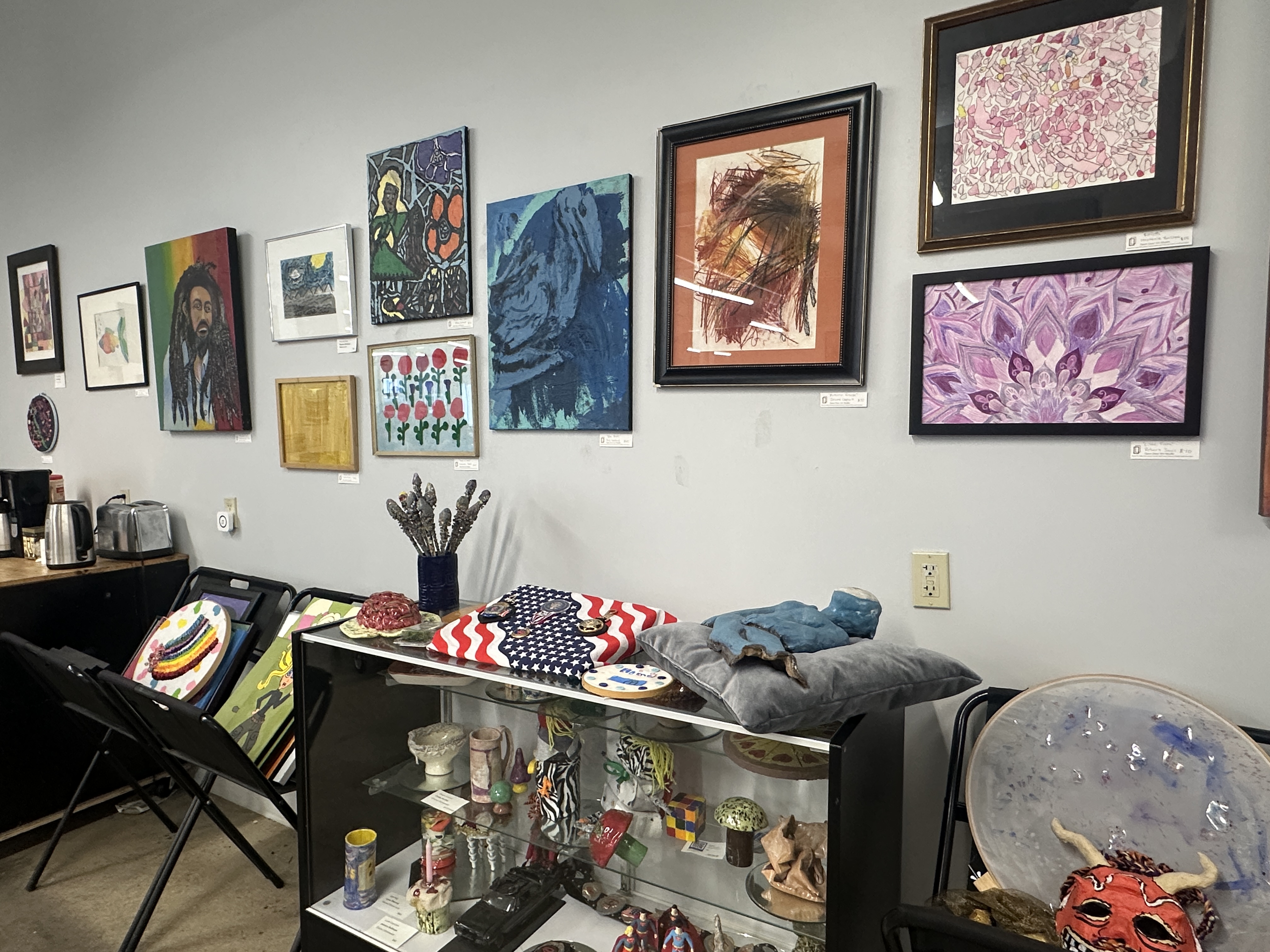 wall with many framed paintings and a shelf of various small sculptures