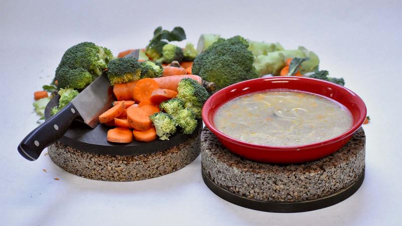 Two Cork Rounds are topped with a spread of vegetables, a knife, and a bowl of soup.