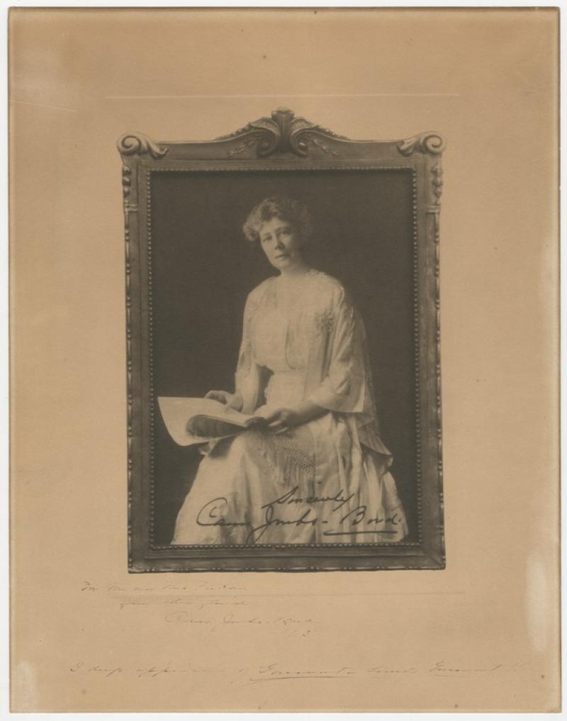 A sepia photograph of Carrie Jacobs Bond seated and holding paper