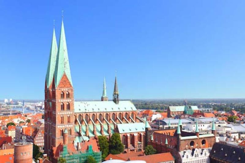 A orange brick church with light green steeples against a bright blue sky
