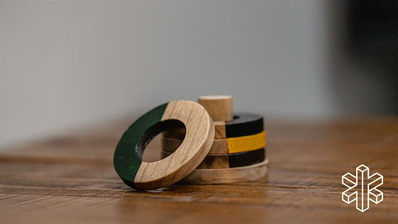 A small wooden circle with a hole in the middle, half painted black, leans against four other similar wooden circles stacked on a wooden peg.