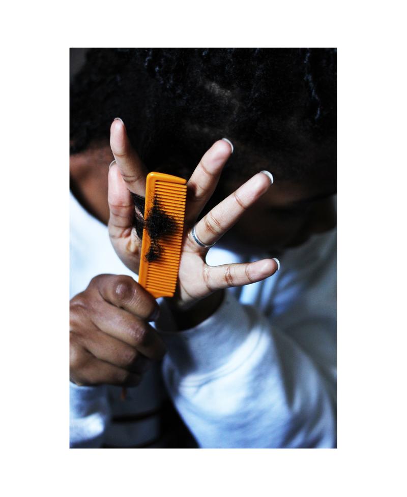 Black woman combing her hair while sitting on ground.