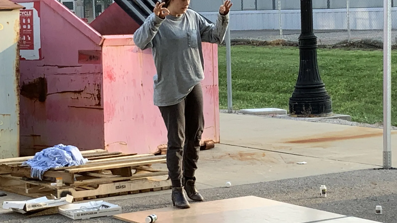 A woman performs a tap dance in front of a dumpster.