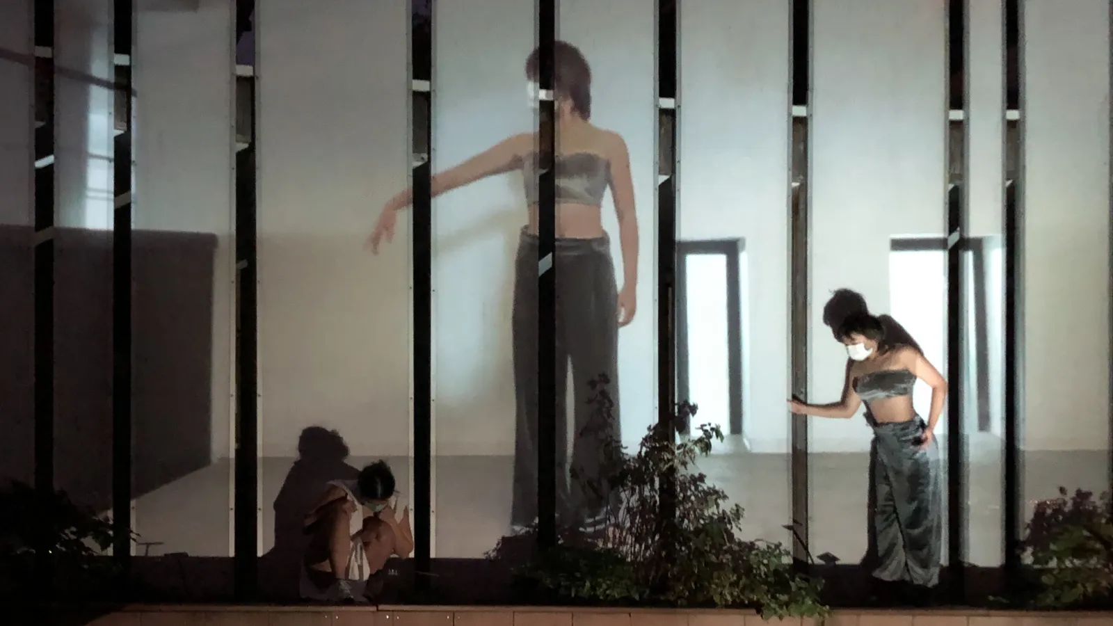 figures mid-dance, a pre-recorded video of them dancing is also being projected on the wall behind them