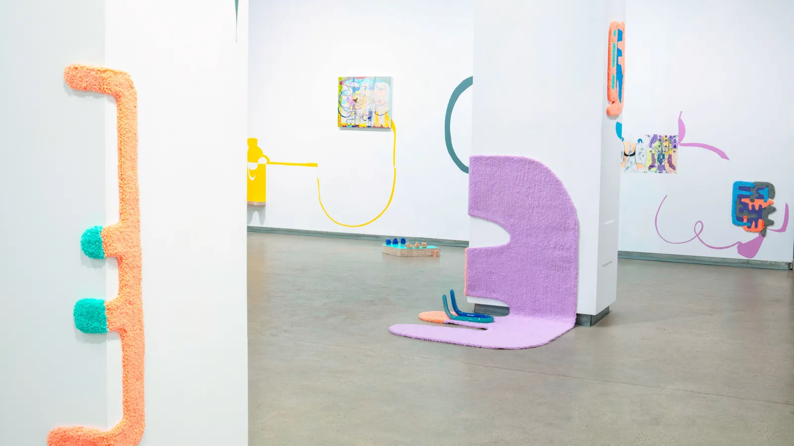artwork of colorful rugs in various sizes and shapes are displayed among paintings in a gallery setting