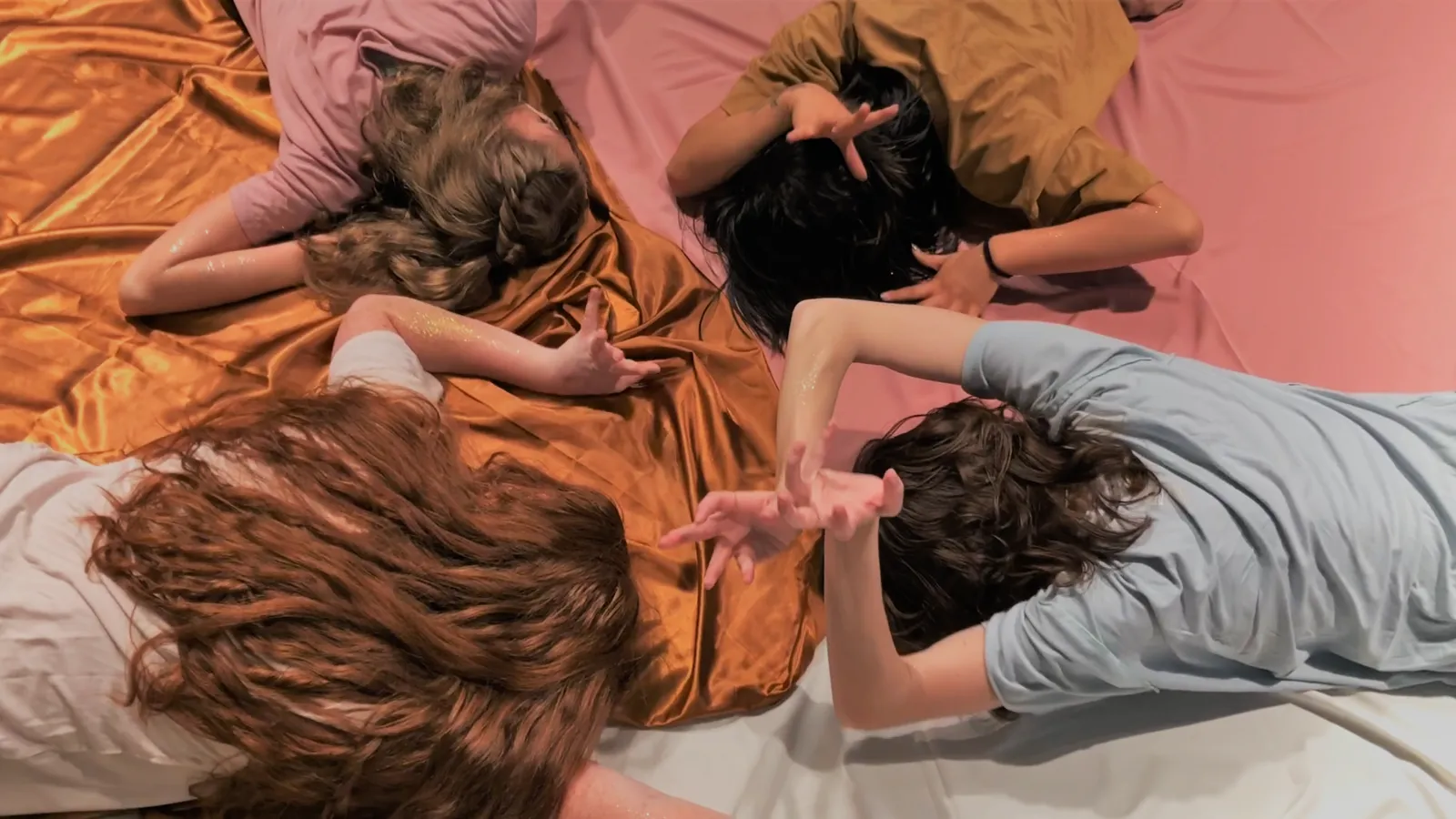 Four people laying facedown on colored fabric.