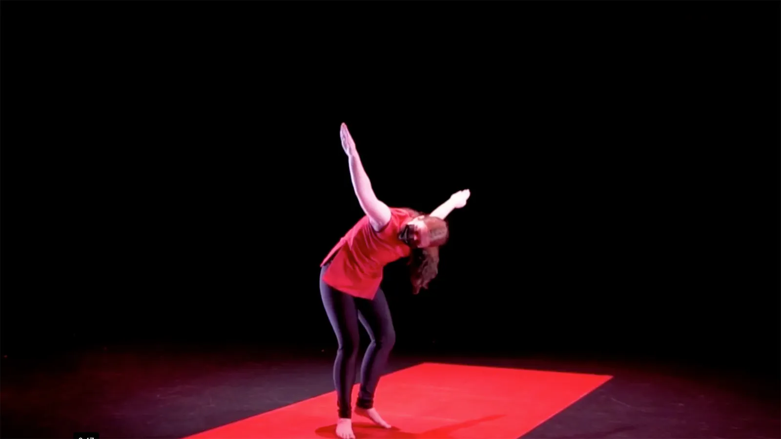 A dancer poses on a red floor in front of a black background.