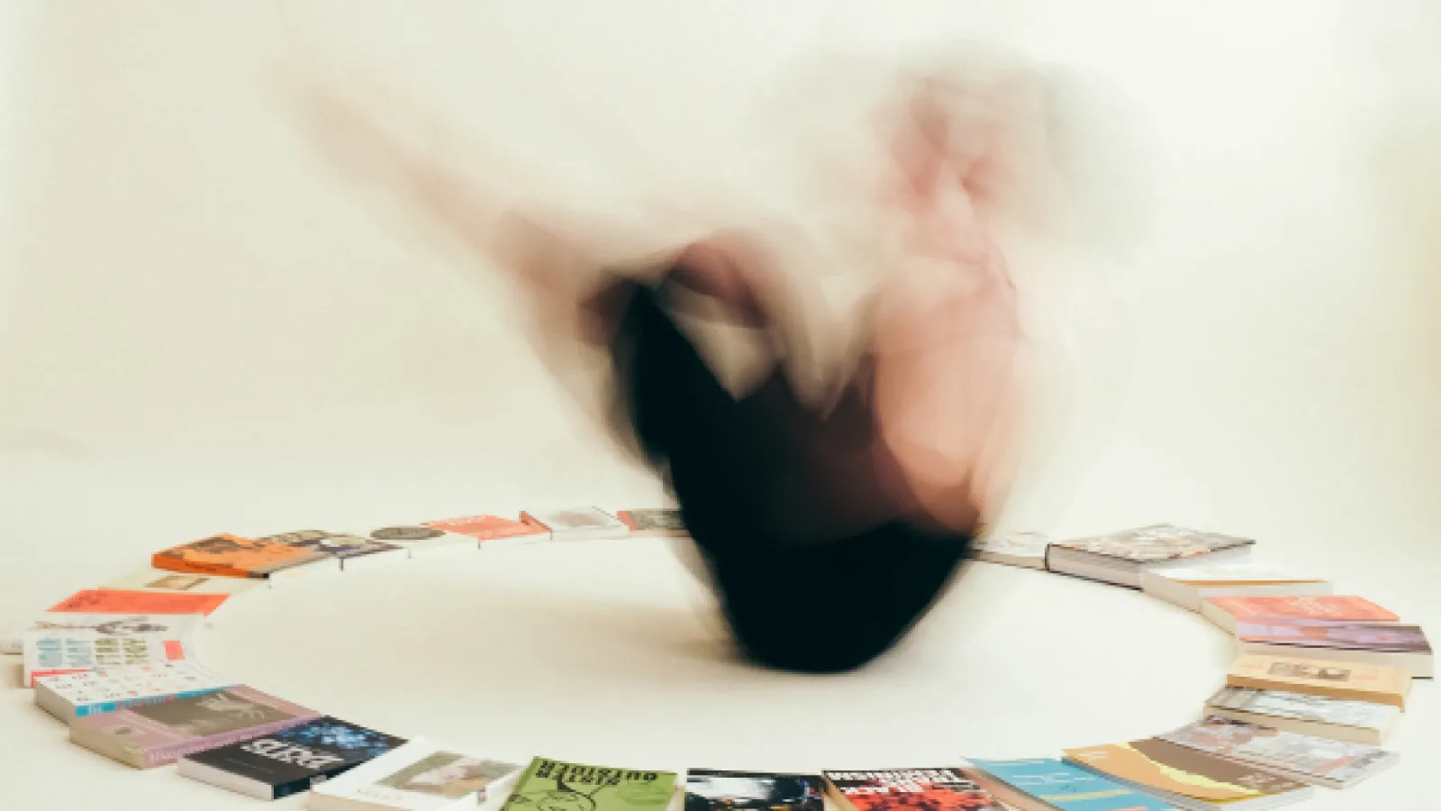 Person spinning/dancing in the center of a circle of books Photo by Kate Sweeney