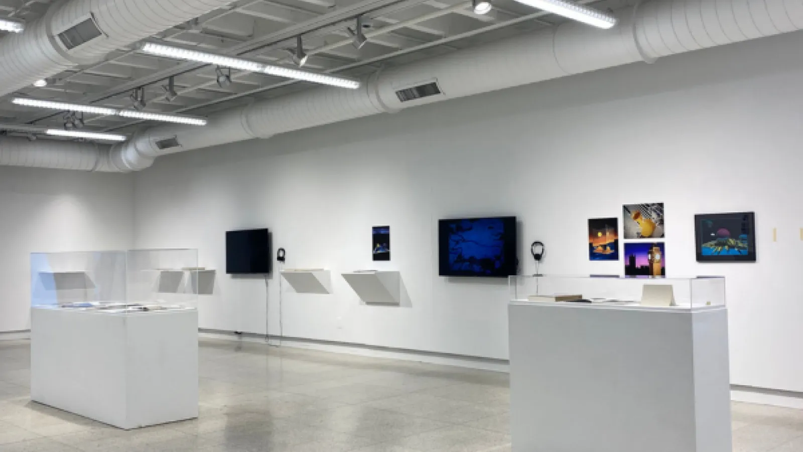 Exhibit at Hopkins Hall, featuring two pedestals with books and magazines, two tv’s on the wall, and artwork on the wall.