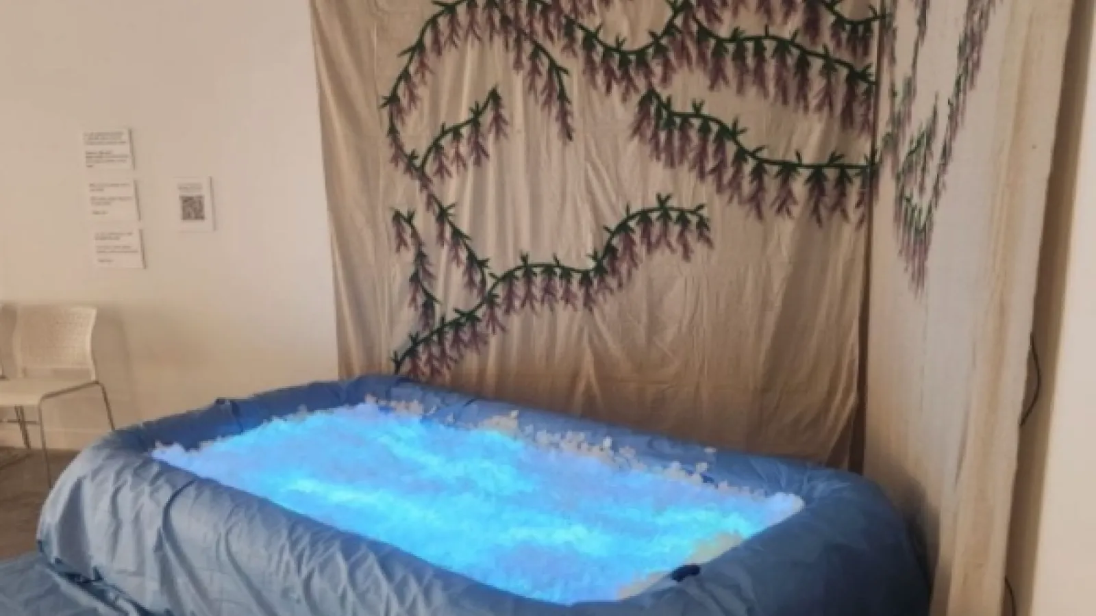A glowing bue pool filled with fake flower petals and a painting of wisteria flowers behind it