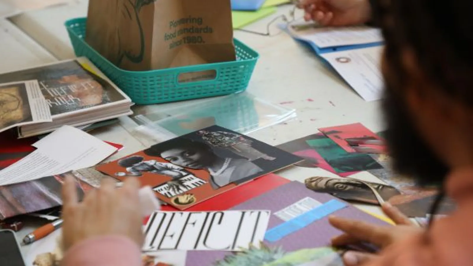 A picture taken over a person's shoulder, on the table in front of them are collage-making materials