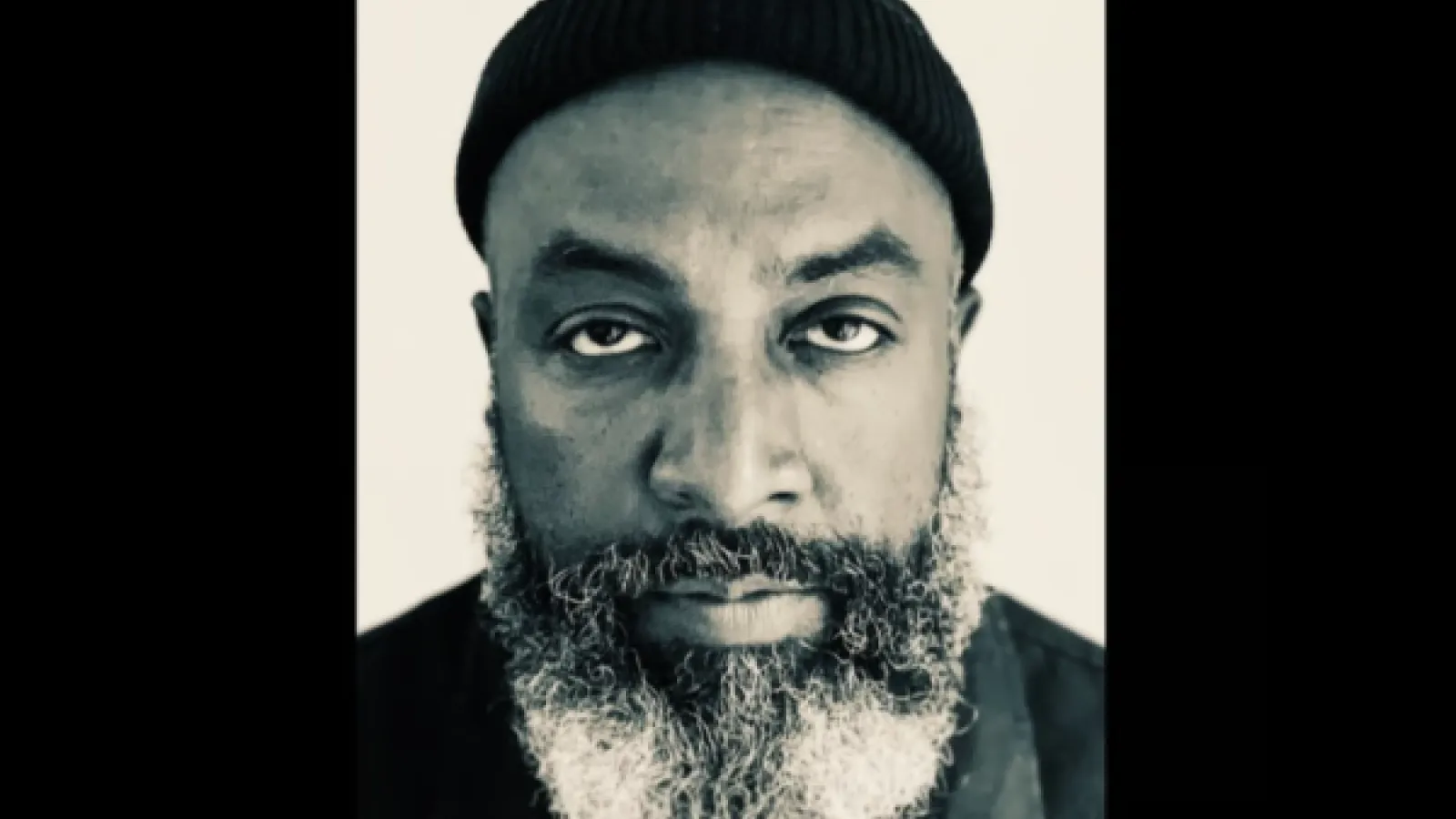 A black-and-white photo portrait of poet Roger Robinson, looking towards the camera.