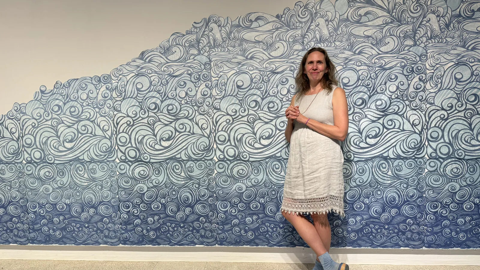 Melissa standing in front of her piece The Flood, featuring swirling blue wallpaper