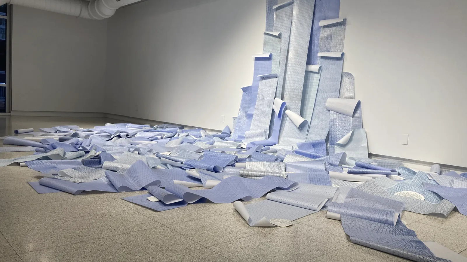 Flood of blue printed paper spilling down the gallery wall like a waterfall