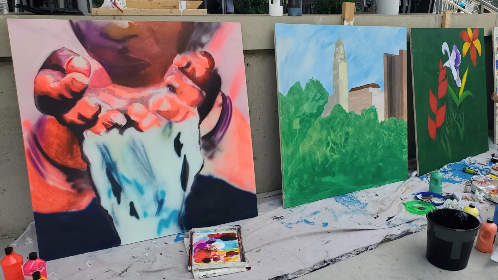 three square paintings, including hands with water and the Columbus skyline