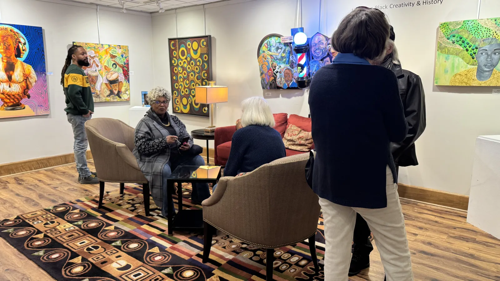 Visitors exploring an art gallery, engaged in viewing and discussing the colorful paintings on the walls.