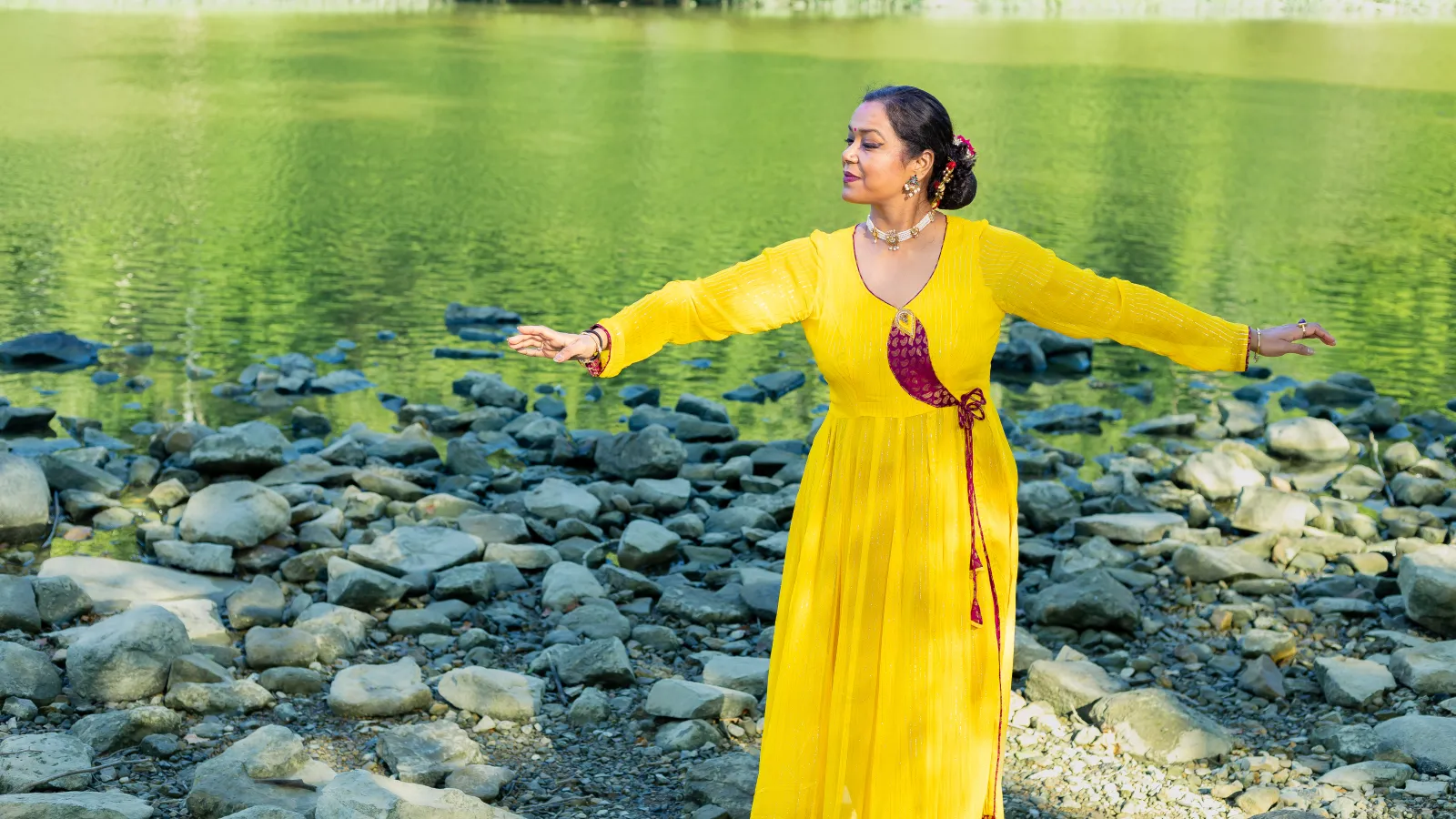 a woman in a yellow traditional Indian outfit dancing beside water