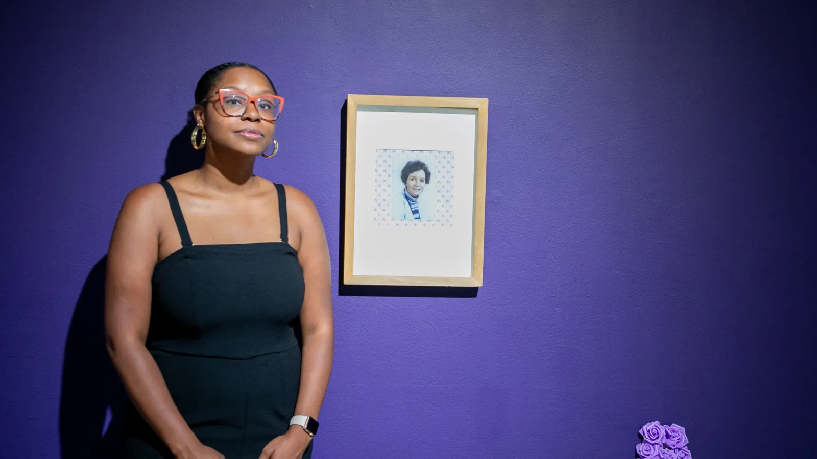 Ajanae standing next to a photo of her grandmother against a purple wall