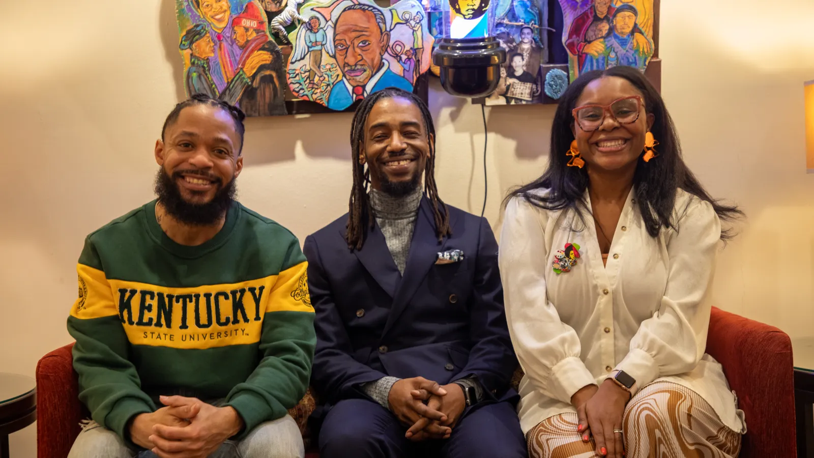 terron, arris, and ajanae smiling on a couch in front of a colorful piece of artwo