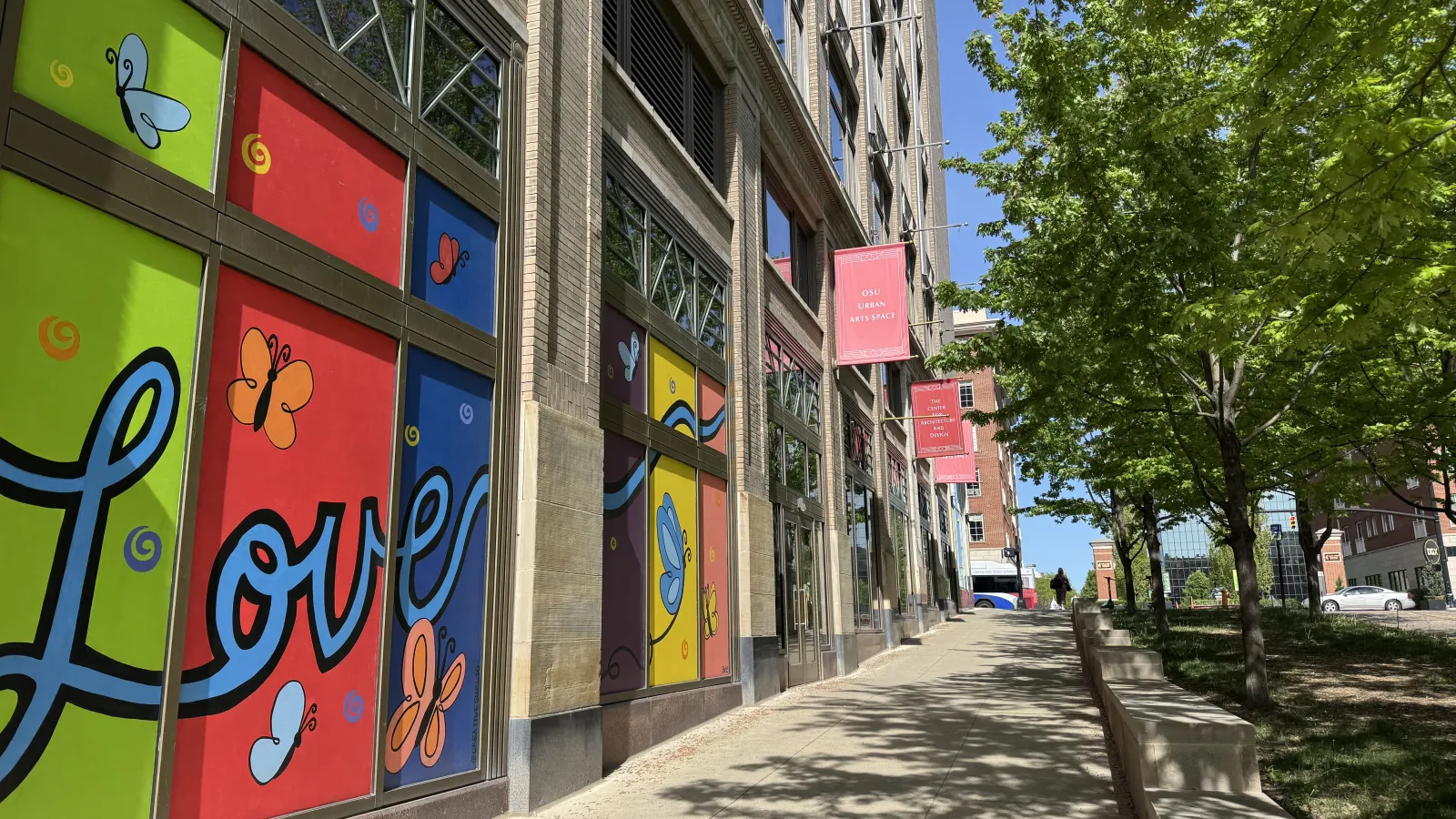 Lazarus building windows with Love painted on one side, trees on the other, and red banners that say OSU Urban Arts Space